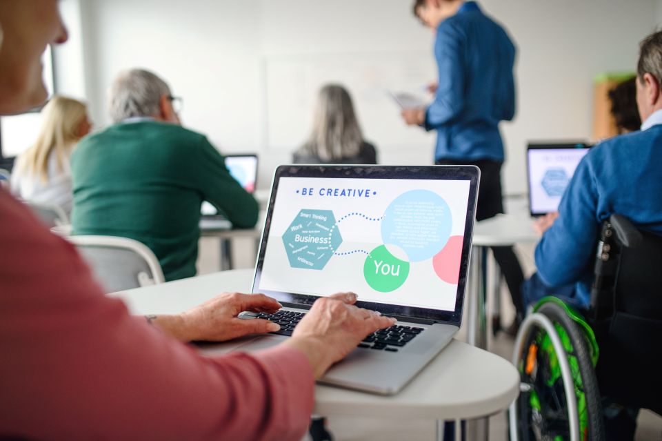 Personne utilisant un ordinateur lors d’une formation, dans un groupe incluant un participant en fauteuil roulant.
