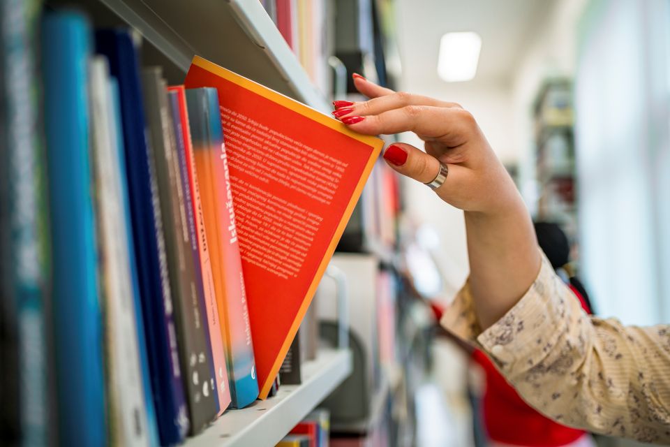 Personne sélectionnant un ouvrage dans une bibliothèque de ressources pédagogiques.