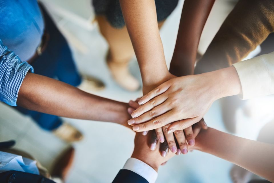 Mains de plusieurs personnes superposées pour symboliser l’esprit d’équipe, la coopération et l’engagement collectif.